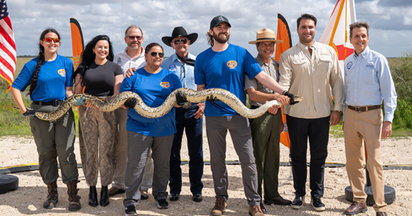 Group of people outdoors holding a large python snake