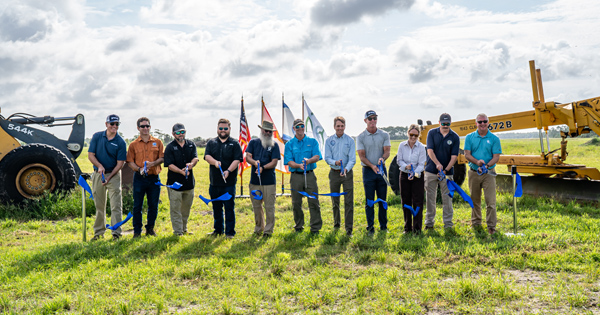 A group of people participating in an outdoor ribbon cutting ceremony